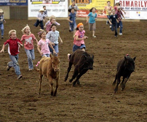 A group of children running around horses in the dirt.